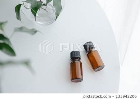 Brown bottles of essential oils and houseplants lined up on a white table, creating a natural and minimalist image 133942206