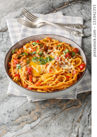 Taco spaghetti fusion food with green chili, cheese, tomatoes, spices close-up in a plate. Vertical 133942355