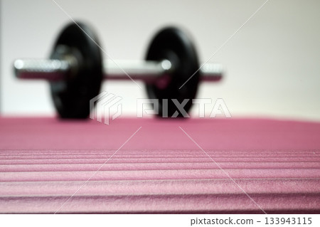Indoor. A small dumbbell placed on a yoga mat Indoor. A small dumbbell placed on a yoga mat 133943115