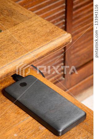 Indoor. power bank placed on the corner of a wooden desk 133943116
