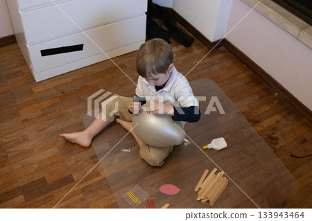 Young boy decorating balloon with craft supplies on floor Young boy decorating balloon with craft supplies on floor 133943464