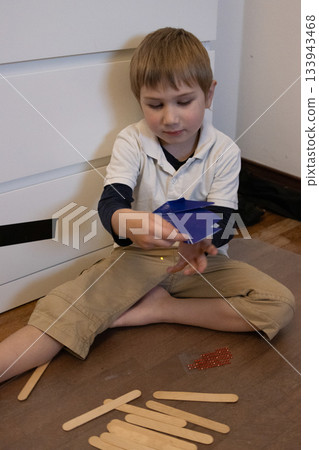 Young boy creating craft with paper and sticks 133943468