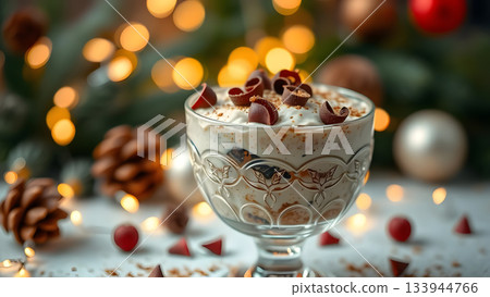 A festive dessert parfait in a glass goblet, topped with chocolate curls, sits amidst pinecones and ornaments, with warm lights in the background 133944766