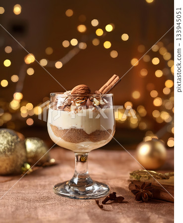 A layered dessert in a glass, topped with cocoa powder and a cinnamon stick, amidst a warm, festive setting A layered dessert in a glass, topped with cocoa powder and a cinnamon stick, amidst a warm, festive setting 133945051