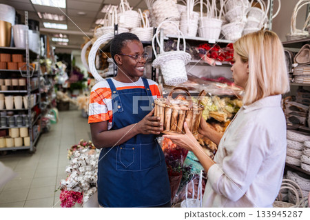 Smiling florist handing wicker basket to customer in flower shop 133945287