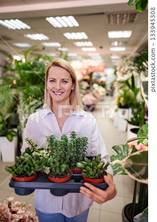 Florist Holding a Tray of Succulents Smiling at the Camera in a Flower Shop 133945308