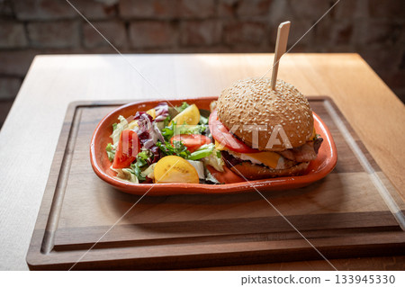 Delicious gourmet burger served with fresh vegetables on a wooden table Delicious gourmet burger served with fresh vegetables on a wooden table 133945330