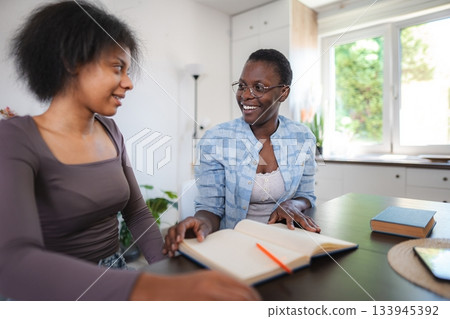 Mother and Daughter Studying Together at Home, Sharing a Book and Smiling Mother and Daughter Studying Together at Home, Sharing a Book and Smiling 133945392