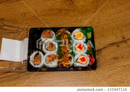 Set of sushi rolls in plastic box on wooden table. Sushi for take away or delivery of sushi in plastic container Set of sushi rolls in plastic box on wooden table. Sushi for take away or delivery of sushi in plastic container 133947110