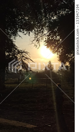 A solitary figure admires a tranquil twilight landscape, immersed in the warm hues of the setting sun. This serene scene evokes contemplation and inspiration, ideal for travel themes. 133947194