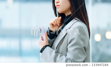 A woman/businesswoman thinking with a smartphone A woman/businesswoman thinking with a smartphone 133947284