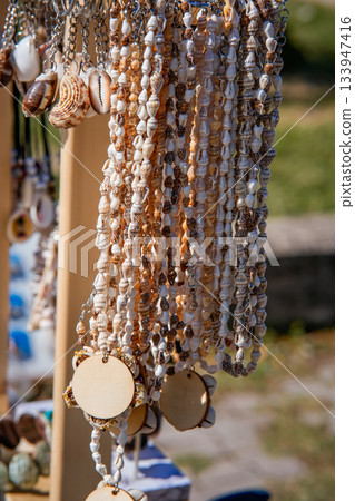 Close-up view of a handmade seashell hanging decoration displayed in a souvenir shop. Detailed texture of natural shells, artisanal craftsmanship, and coastal tourist atmosphere. Suitable for themes Close-up view of a handmade seashell hanging decoration displayed in a souvenir shop. Detailed texture of natural shells, artisanal craftsmanship, and coastal tourist atmosphere. Suitable for themes 133947416