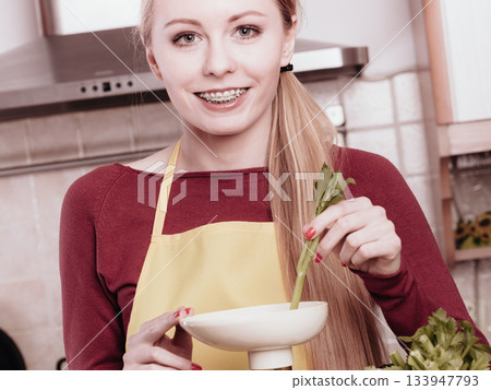 Woman in kitchen making vegetable smoothie juice 133947793