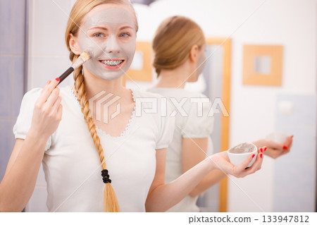 Woman applying with brush clay mud mask to her face Woman applying with brush clay mud mask to her face 133947812