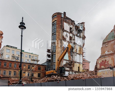 large building is being demolished by a large excavator.  133947868