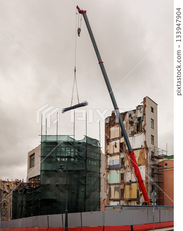 large building is being demolished by a large excavator. large building is being demolished by a large excavator. 133947904
