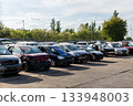 Rows of dismantled cars stand on open yard, showing missing parts, broken fronts  exposed interiors. Scene reflects scrapyard atmosphere scattered vehicles, warm sunlight and industrial surroundings 133948003