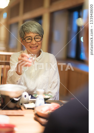 在日式旅館，一對老年夫婦在晚餐時為客人斟酒，溫馨的一幕。 133948600