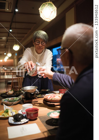 在日式旅館，一對老年夫婦在晚餐時為客人斟酒，溫馨的一幕。 133948612