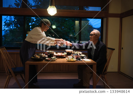 在日式旅館，一對老年夫婦在晚餐時為客人斟酒，溫馨的一幕。 133948614