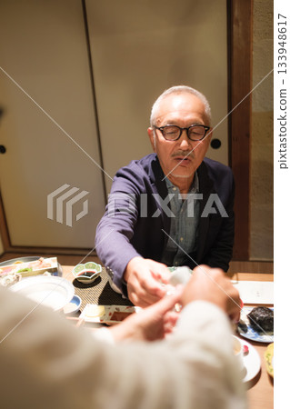 在日式旅館，一對老年夫婦在晚餐時為客人斟酒，溫馨的一幕。 133948617