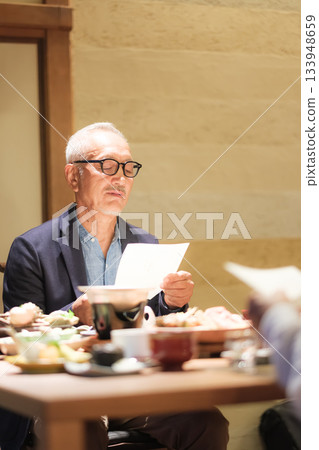A senior couple enjoys dinner at a traditional Japanese inn while looking at the menu. 133948659
