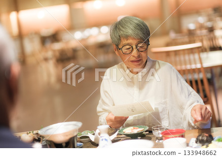 一對老年夫婦在一家傳統的日式旅館裡一邊享用晚餐一邊查看菜單。 133948662