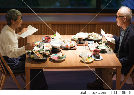 一對老年夫婦在一家傳統的日式旅館裡一邊享用晚餐一邊查看菜單。 133948666