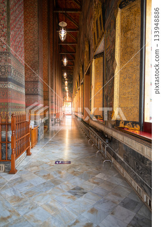 Sunlit corridor inside the main hall of Wat Pho in Bangkok, with ornate patterned walls and warm light streaming through the doorway, creating a peaceful atmospheric scene. 133948886