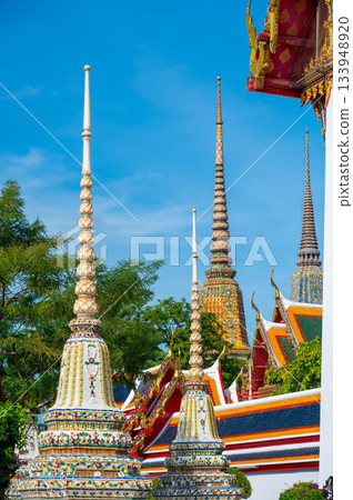 Exterior view of Wat Pho with richly decorated stupas covered in colorful floral ceramics and golden temple roofs shining under a clear blue sky on a bright sunny day in Bangkok. Exterior view of Wat Pho with richly decorated stupas covered in colorful floral ceramics and golden temple roofs shining under a clear blue sky on a bright sunny day in Bangkok. 133948920