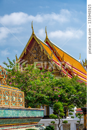 Exterior view of Wat Pho with richly decorated stupas covered in colorful floral ceramics and golden temple roofs shining under a clear blue sky on a bright sunny day in Bangkok. Exterior view of Wat Pho with richly decorated stupas covered in colorful floral ceramics and golden temple roofs shining under a clear blue sky on a bright sunny day in Bangkok. 133948925
