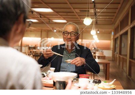 一對老年夫婦在慶祝60歲生日的旅途中，於一家傳統的日本旅館悠閒地享用晚餐。 133948956