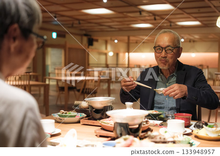 一對老年夫婦在慶祝60歲生日的旅途中，於一家傳統的日本旅館悠閒地享用晚餐。 133948957