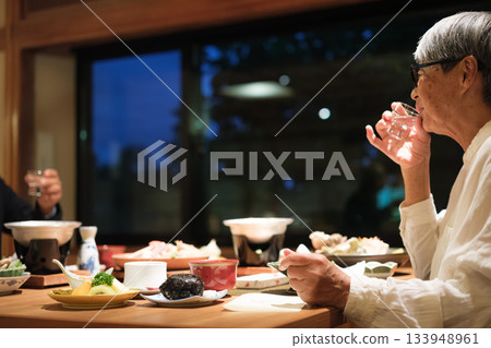 A senior couple enjoying a leisurely dinner at a traditional Japanese inn on a trip to celebrate their 60th birthday. A senior couple enjoying a leisurely dinner at a traditional Japanese inn on a trip to celebrate their 60th birthday. 133948961