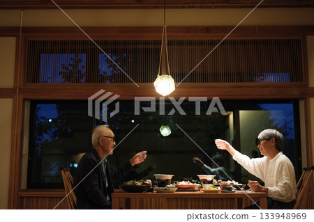 一對老年夫婦在慶祝60歲生日的旅途中，於一家傳統的日本旅館悠閒地享用晚餐。 133948969