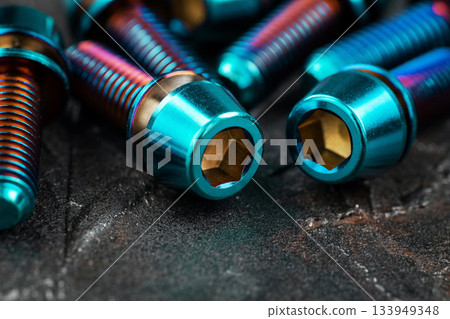 Blue titanium screws in a row with a hexagon head on a black textured background close-up Blue titanium screws in a row with a hexagon head on a black textured background close-up 133949348