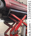 Car lift working on a red vehicle in an auto repair shop during daytime 133949561