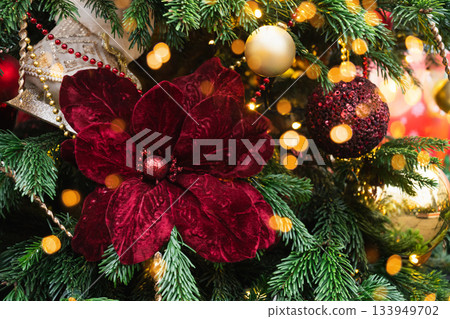 Christmas tree decorated poinsettia flowers and balls with lights garland. Xmas holiday spirit. Winter. Outdoors. 133949702