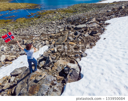 Tourist holds norwegian flag in mountains 133950084