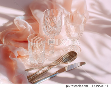 Elegant crystal glassware and cutlery on pastel silk background 133950161