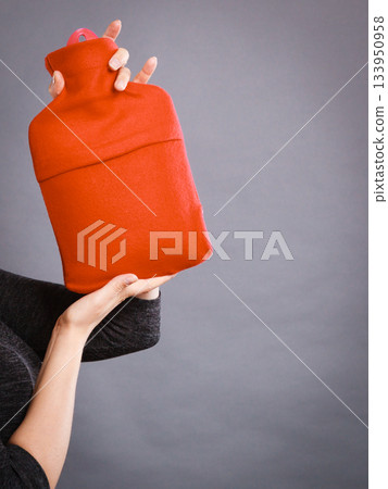 Woman holds hot water bottle in red fleece cover Woman holds hot water bottle in red fleece cover 133950958