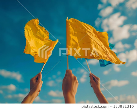 Hands raising yellow flags against blue sky 133951310