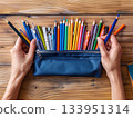 Pencil case with hands on wooden desk 133951314