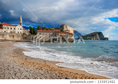Commercial photo of the seafront promenade in Budva, Montenegro, with the historic Old Town and the bell tower of the Cathedral of Saint John the Baptist (Catholic) in the background. Shows boats 133951482