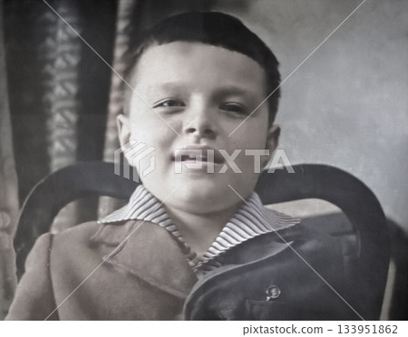 A vintage portrait of a smiling Soviet boy sitting in a chair. Retro photo from the 1970s. 133951862