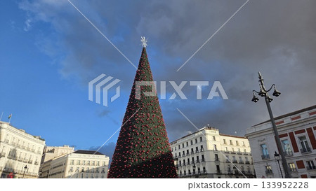 Festive Christmas tree in urban square with dramatic sky for holiday celebration Festive Christmas tree in urban square with dramatic sky for holiday celebration 133952228
