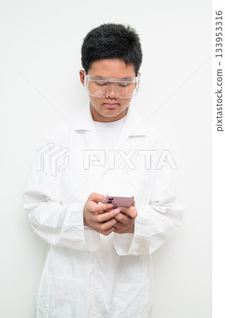 Young Asian Boy Dressed as Scientist with Lab Coat Using Mobile Phone Texting 133953316