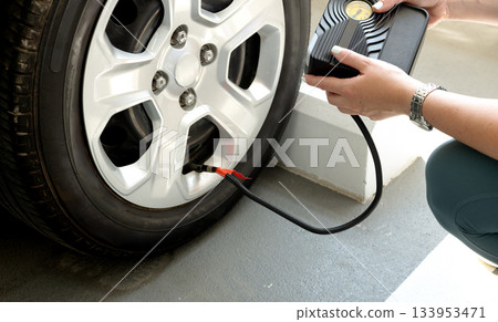 Woman inflating car tire using portable air compressor. Automotive maintenance. 133953471