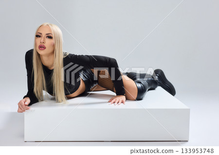 Vivid fashion scene, Dynamic photograph capturing bold fashion and fierce attitude, Fashion model leans against white cube showcasing daring attire and intense expression 133953748