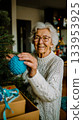 An older woman putting a Christmas ornament on a tree 133953925